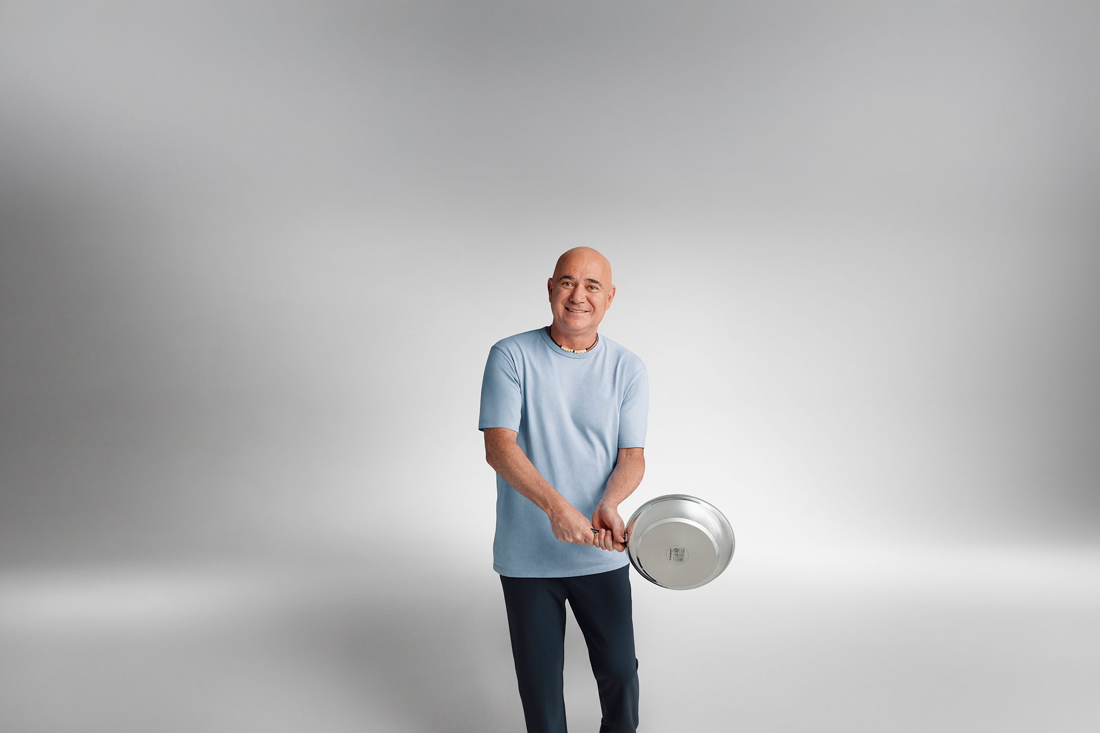 Ο Andre Agassi με ένα μπλε T-shirt κρατάει ένα τηγάνι στα χέρια του.