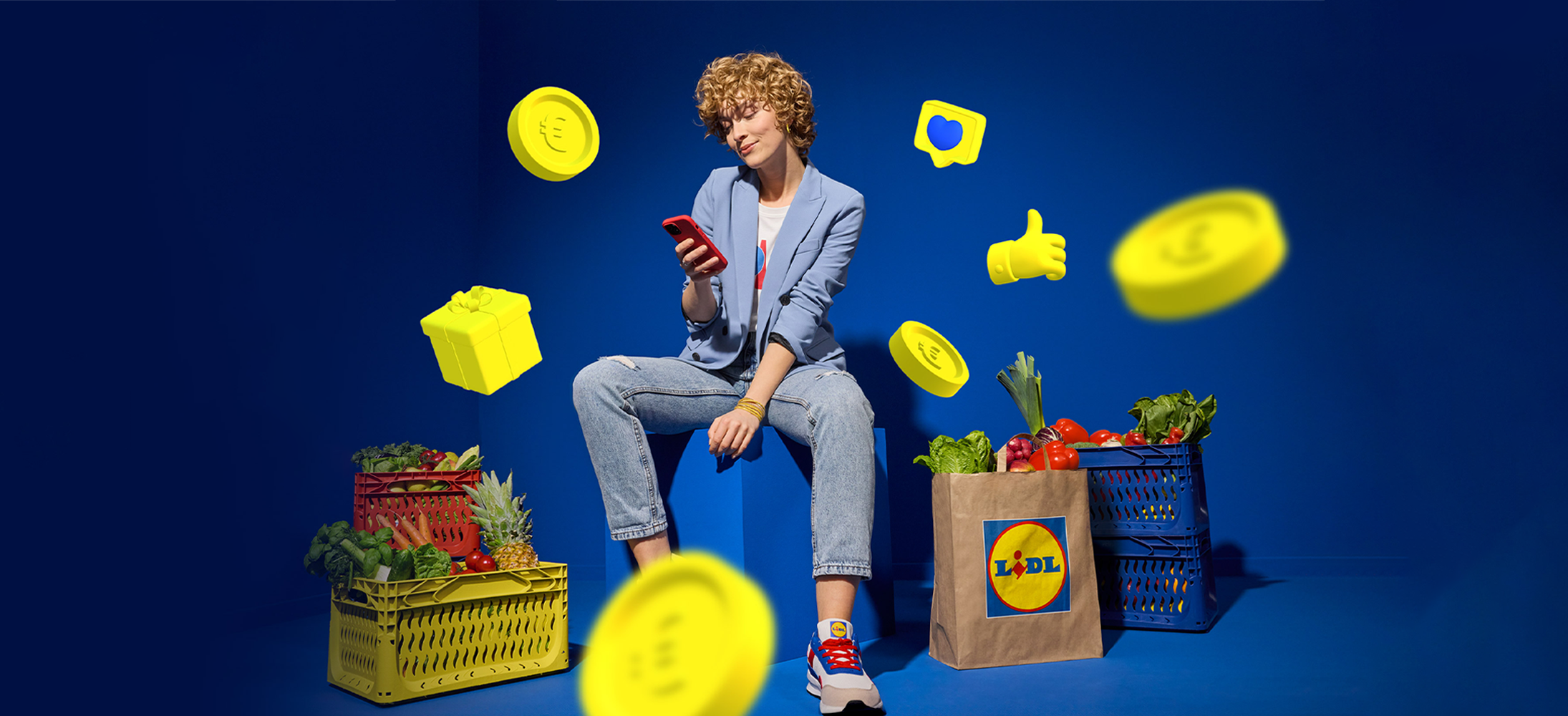 Μια γυναίκα χρησιμοποιεί το κινητό της τηλέφωνο κοντά σε καλάθια με φρούτα και λαχανικά Lidl, με εικονικά νομίσματα και δώρα να αιωρούνται γύρω της.