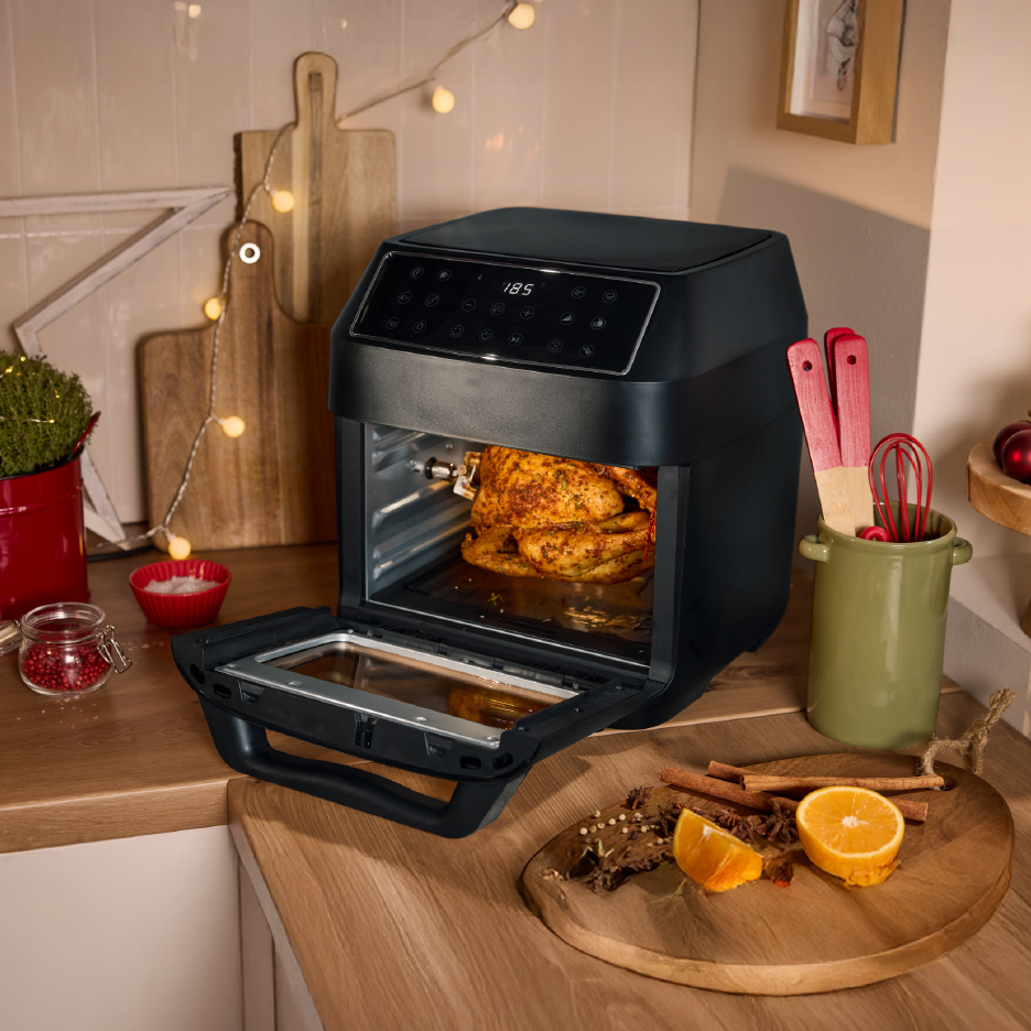 Μαύρη φριτέζα αέρος με κοτόπουλο, σε κουζίνα με χριστουγεννιάτικη διακόσμηση.