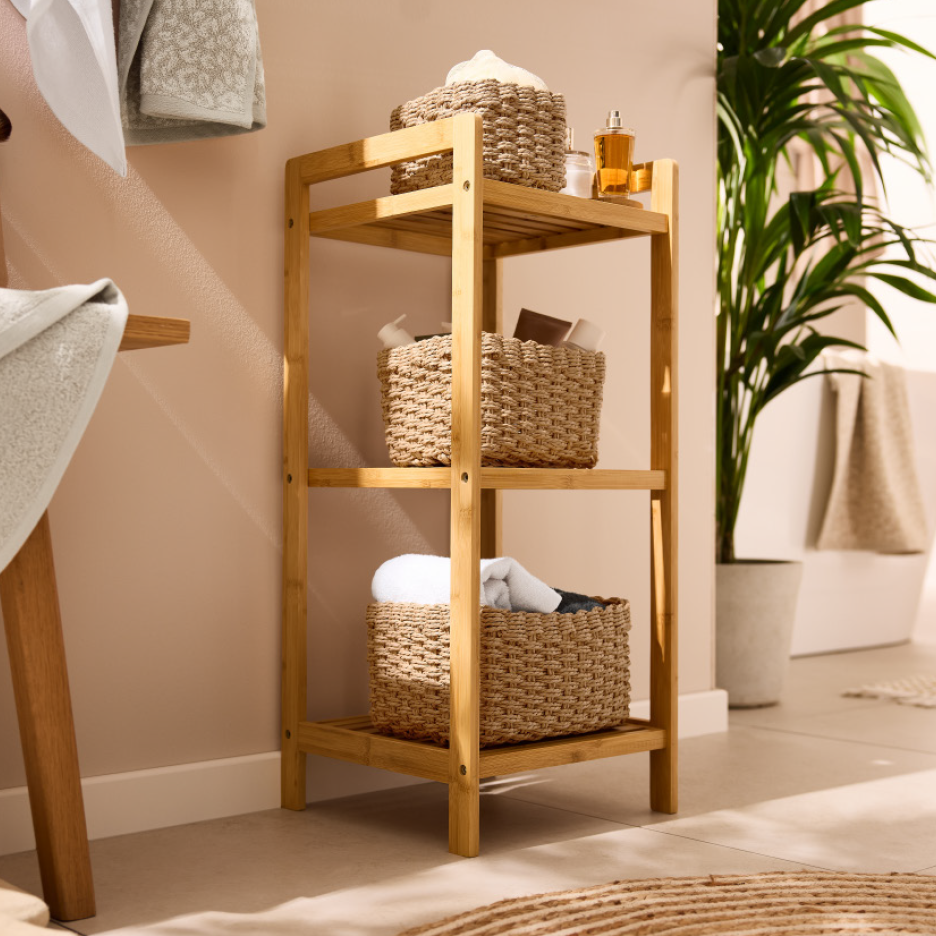Ξύλινη ραφιέρα μπάνιου με ψάθινα καλάθια αποθήκευσης, πετσέτες και προϊόντα περιποίησης.