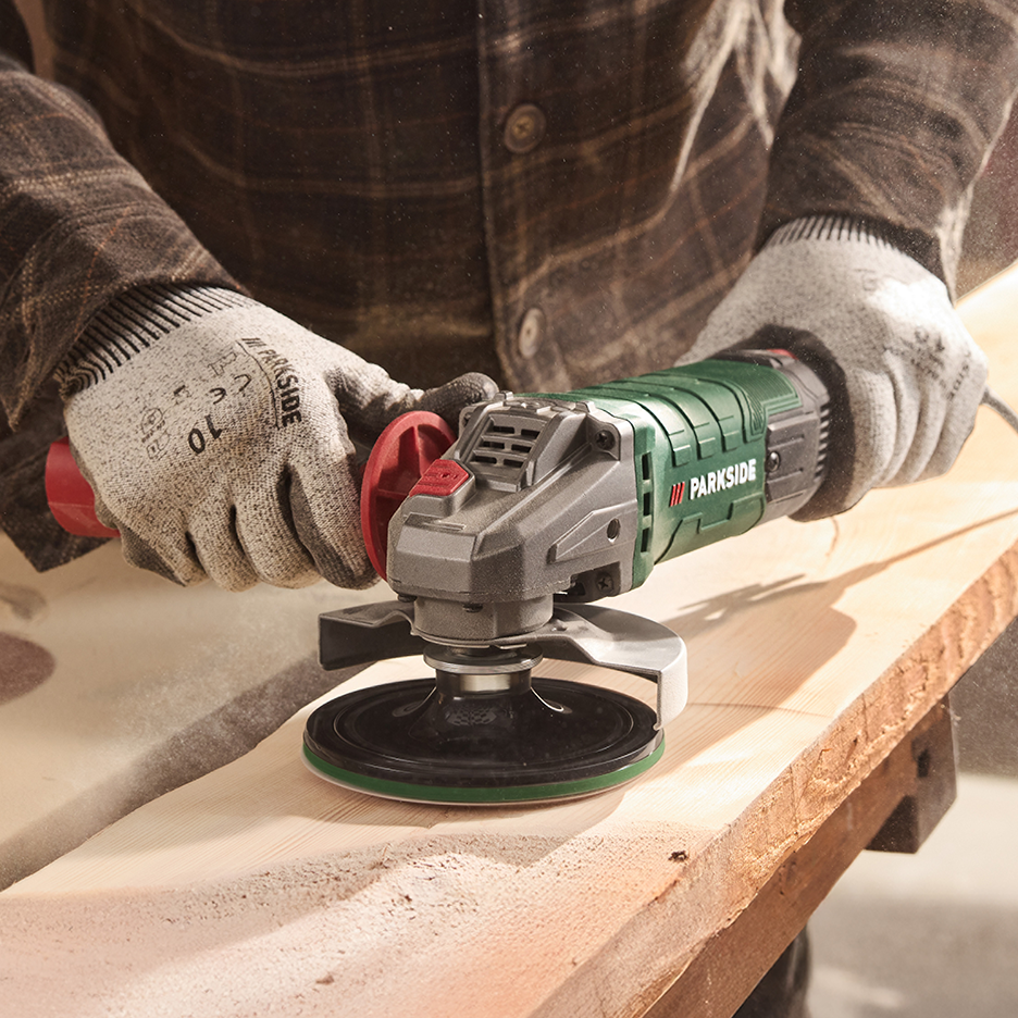 Άνδρας με γάντια χρησιμοποιεί γωνιακό τροχό για να λειάνει μια ξύλινη σανίδα.