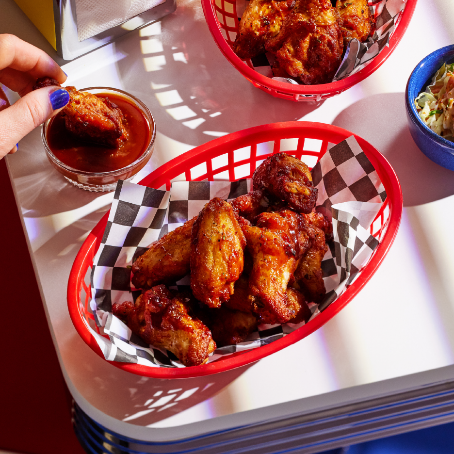 Κοτόπουλο φτερούγες σε κόκκινα καλάθια με σάλτσα και λάχανο σαλάτα σε ένα τραπέζι.