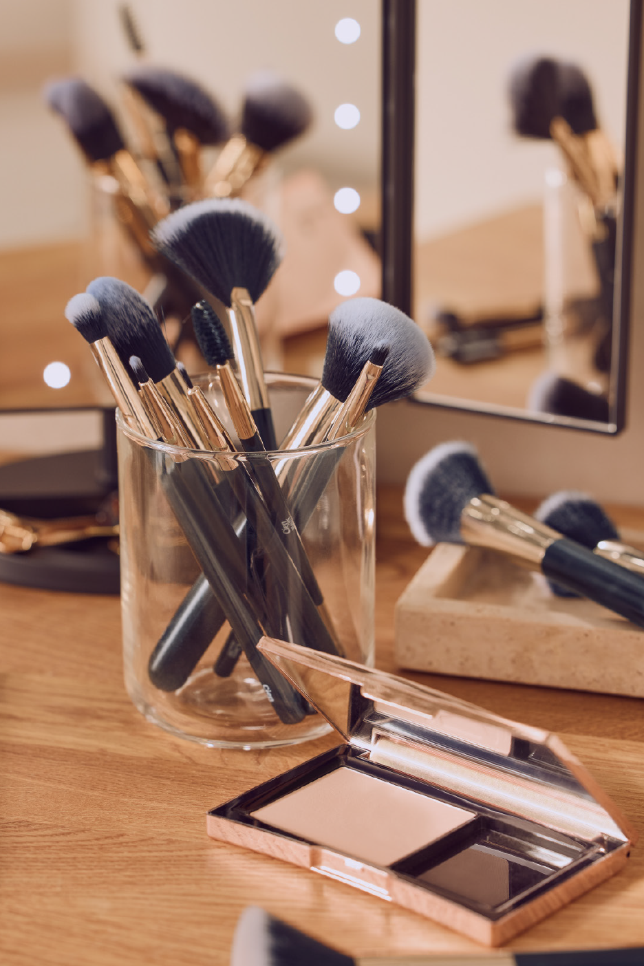 Σετ πινέλων μακιγιάζ σε γυάλινο βάζο και παλέτα μακιγιάζ σε ξύλινη επιφάνεια.