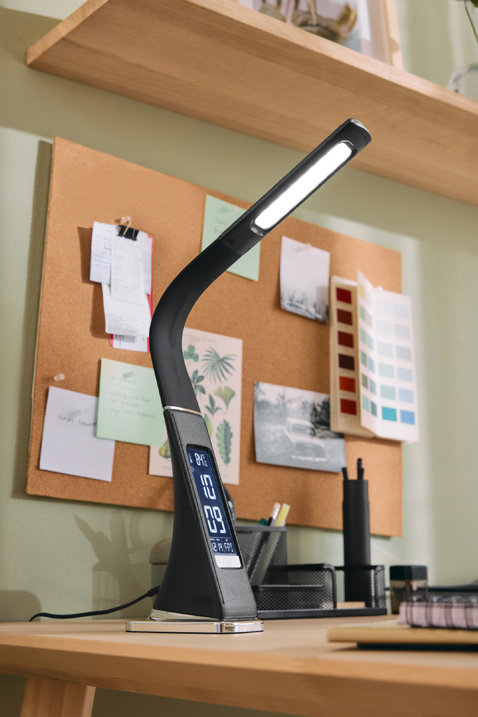 Μαύρο φωτιστικό γραφείου με οθόνη, σε ξύλινο γραφείο με πίνακα ανακοινώσεων.