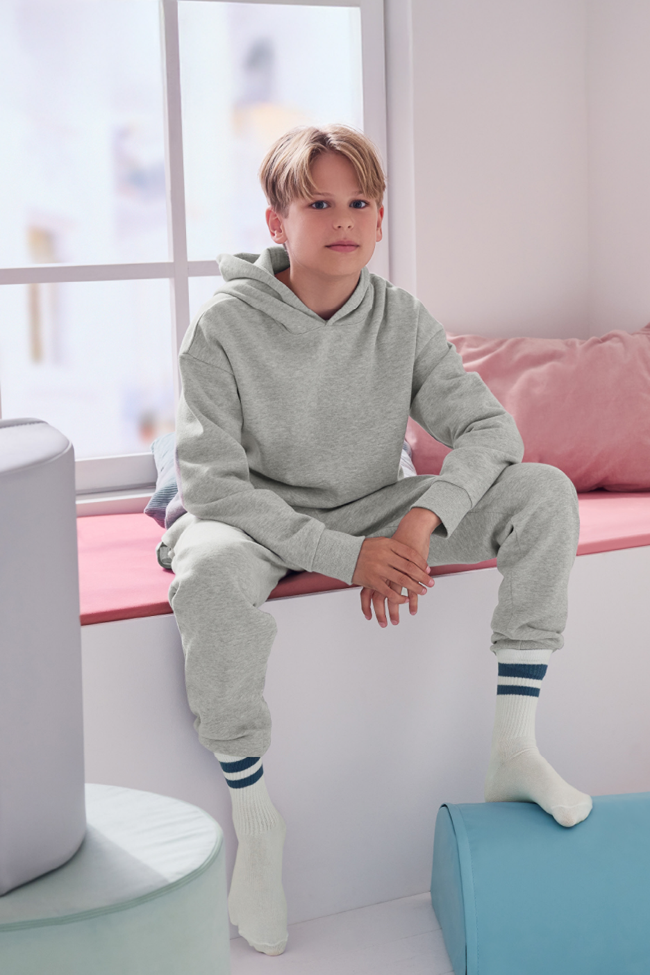 Αγόρι με γκρι φούτερ και παντελόνι φόρμας, κάθεται σε περβάζι παραθύρου.