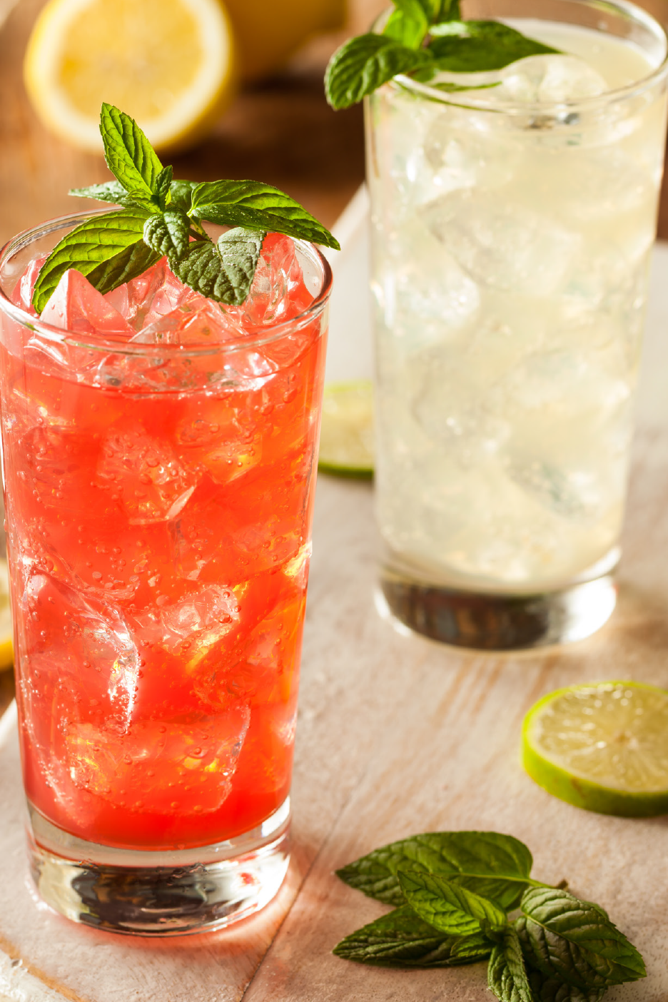 Δύο δροσιστικά κοκτέιλ με μέντα, πάγο και φέτες λάιμ σε ξύλινη επιφάνεια.