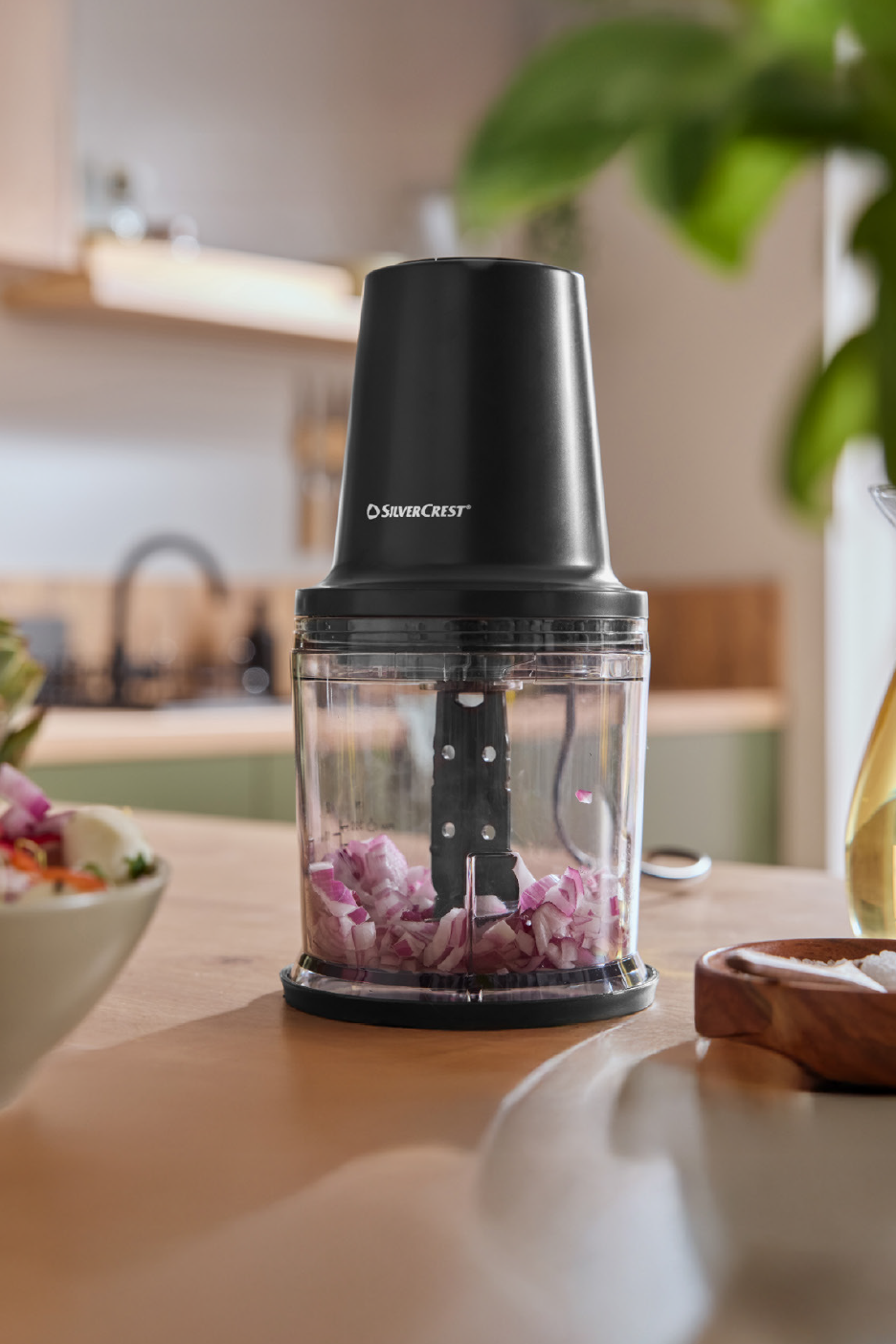 Μαύρος πολυκόφτης SilverCrest με ψιλοκομμένο κρεμμύδι σε ξύλινο πάγκο κουζίνας.