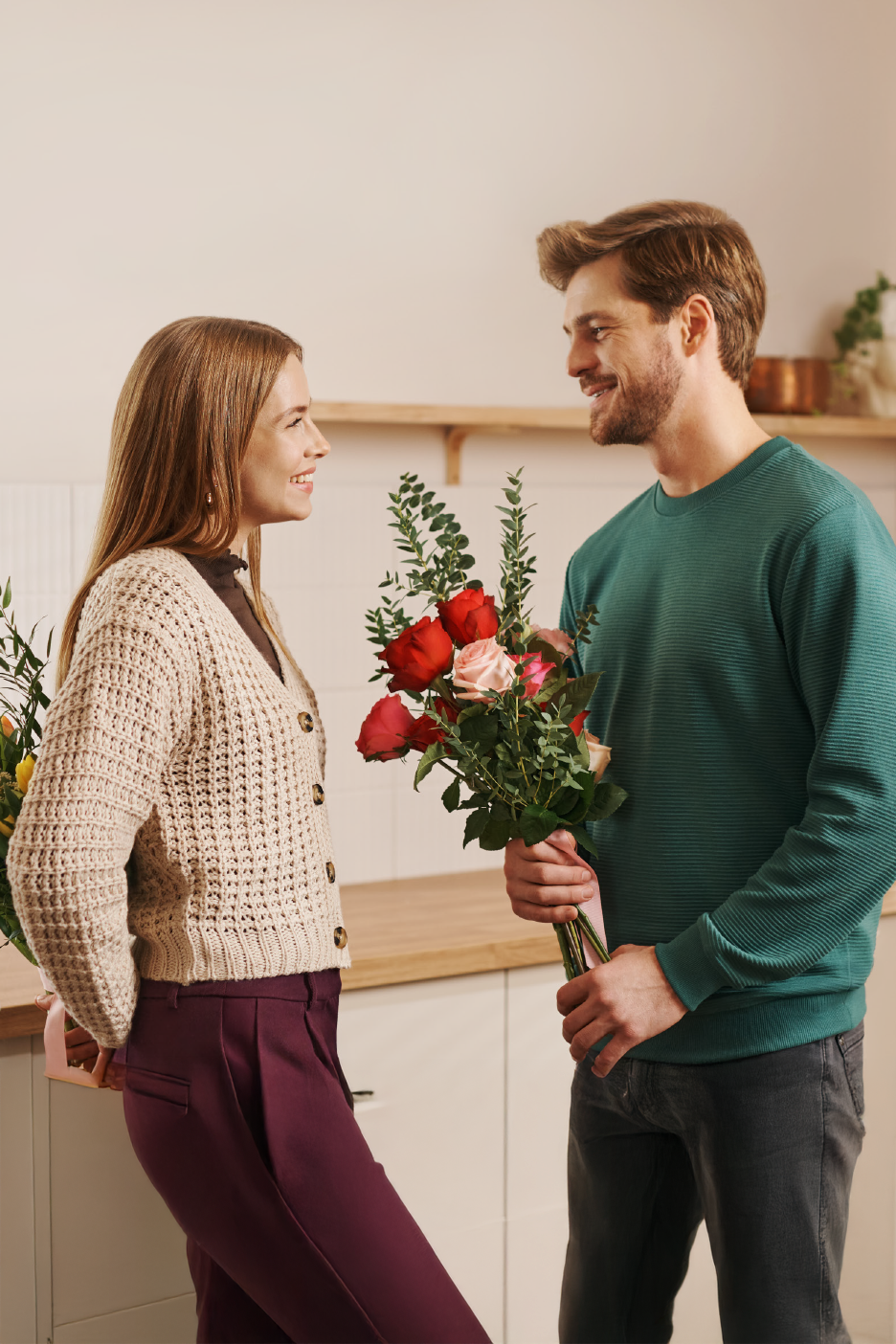 Ένα ζευγάρι χαμογελά ο ένας στον άλλο, κρατώντας ανθοδέσμες με τριαντάφυλλα.