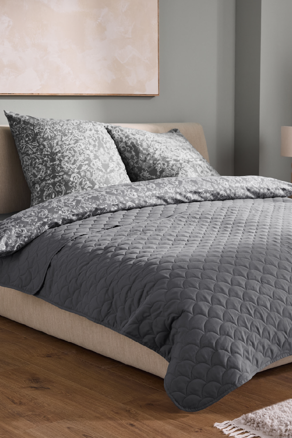 Κρεβάτι με γκρι παπλωματοθήκη με σχέδια, γκρι πάπλωμα και ξύλινο πάτωμα.