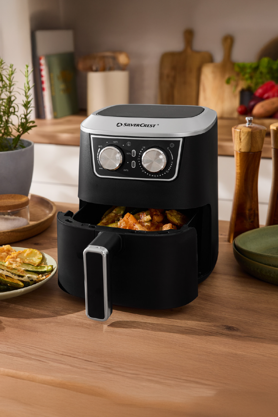 Μαύρη φριτέζα αέρος με ψητά λαχανικά σε ξύλινο πάγκο κουζίνας.