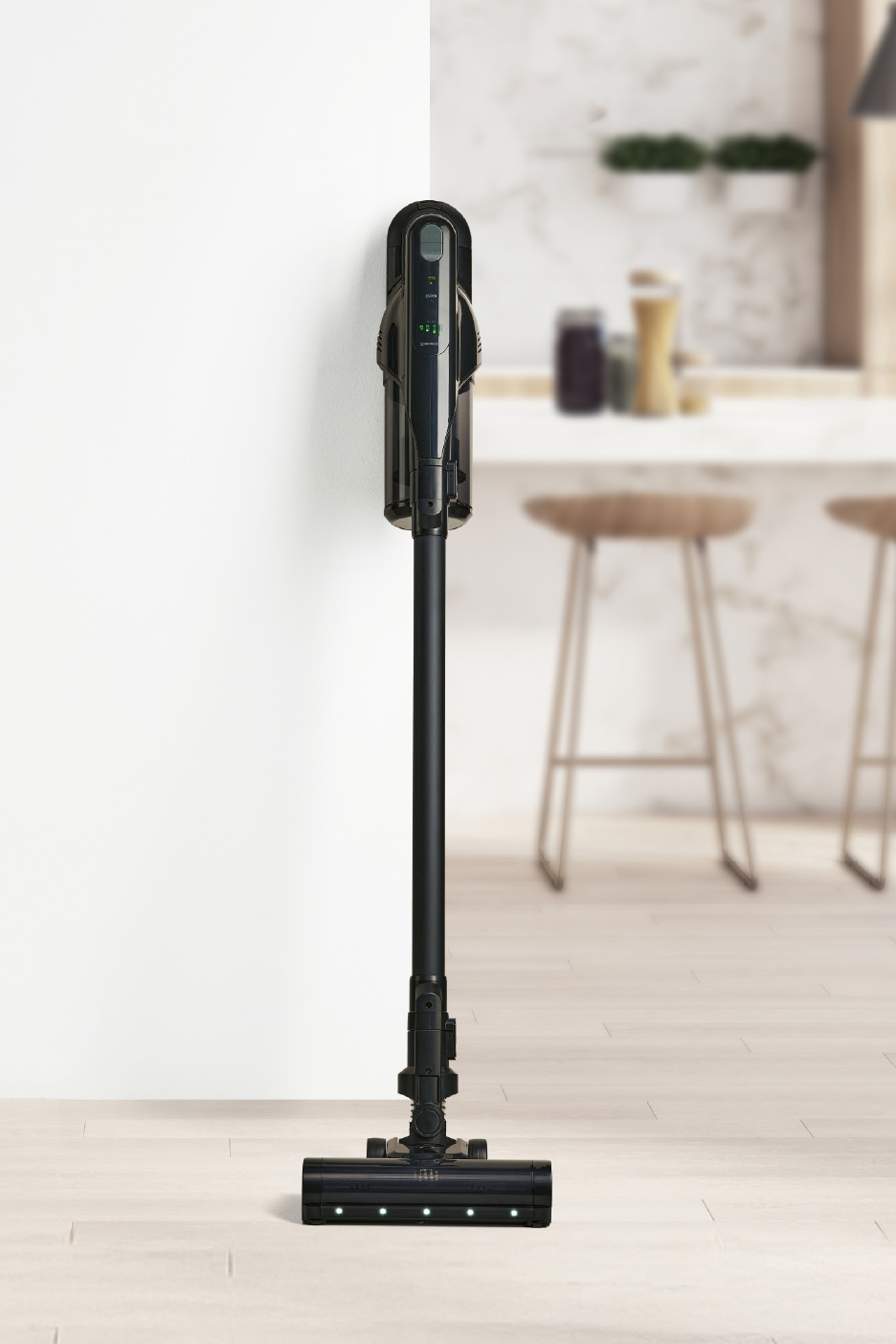 Μαύρη ασύρματη ηλεκτρική σκούπα σε λευκό τοίχο με θολό φόντο κουζίνας.