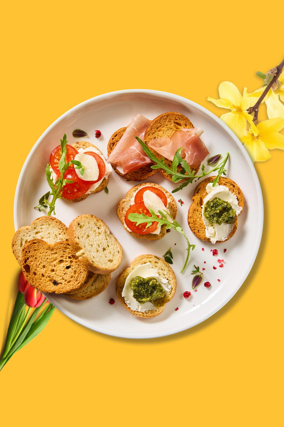 Ποικιλία από μπρουσκέτες με ντομάτα, μοτσαρέλα, προσούτο και πέστο σε λευκό πιάτο.