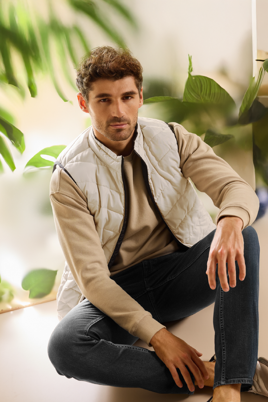 Άνδρας με μπεζ πουλόβερ, λευκό αμάνικο μπουφάν και σκούρο τζιν.