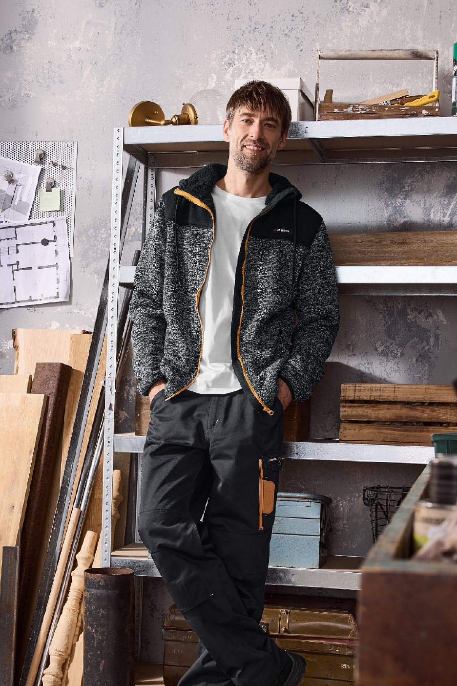 Άνδρας με γκρι φλις ζακέτα και μαύρο παντελόνι εργασίας σε εργαστήριο.