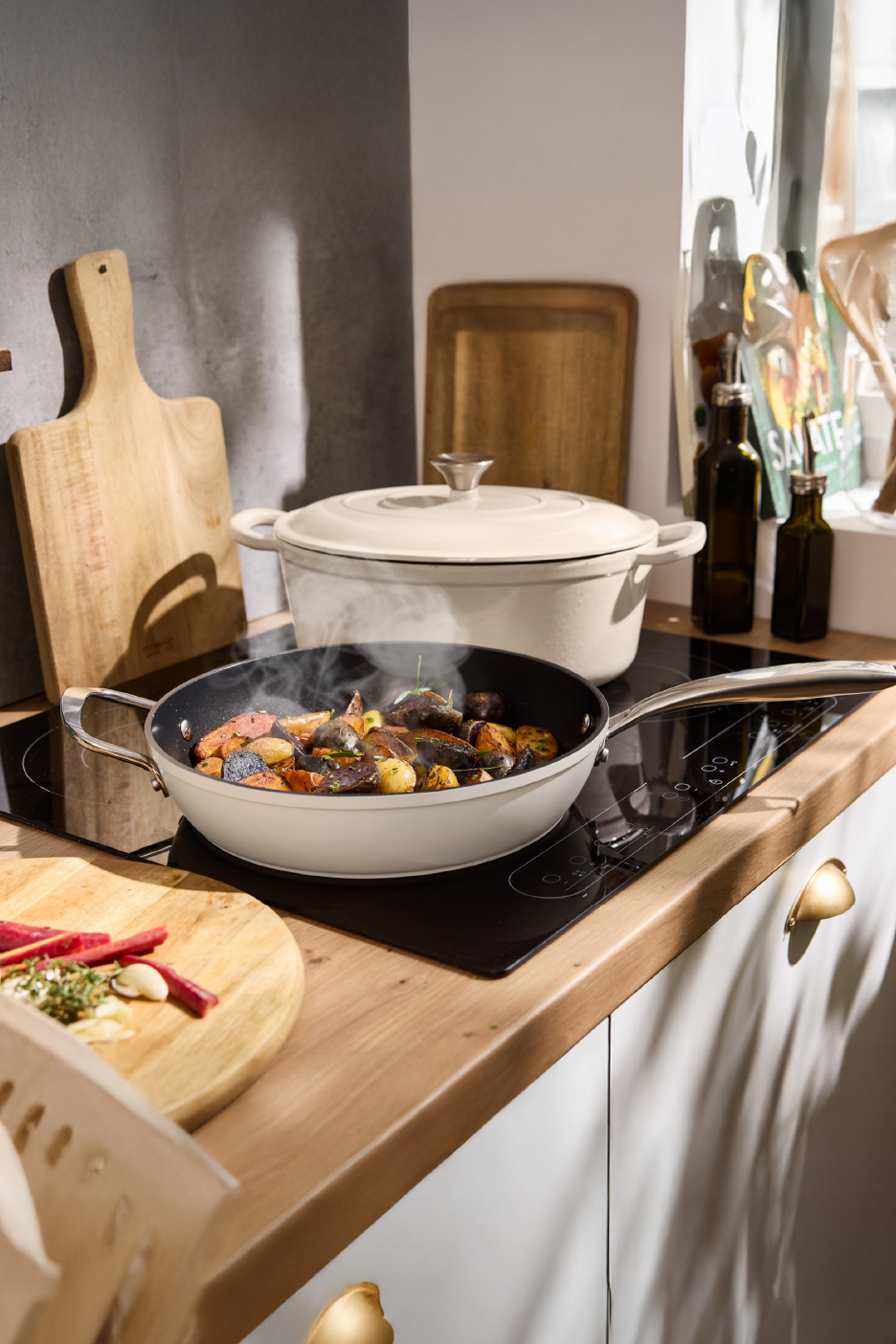Μια κουζίνα με ένα τηγάνι γεμάτο λαχανικά που μαγειρεύονται σε εστία επαγωγής και μια κατσαρόλα.