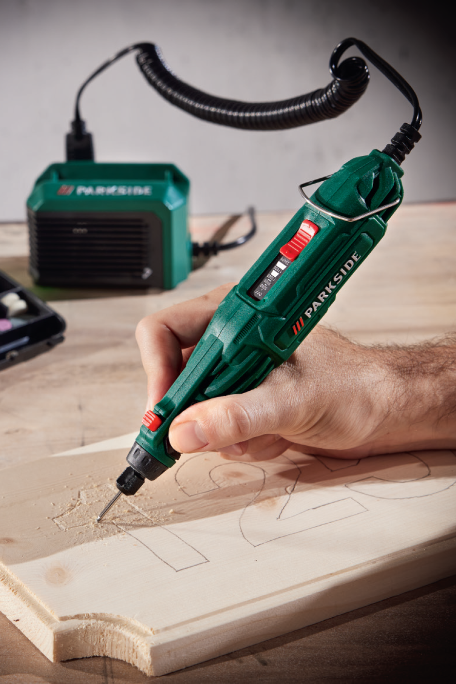 Ένας άνδρας χαράζει ξύλο με ένα πράσινο περιστροφικό εργαλείο, συνδεδεμένο με μια μονάδα ισχύος.