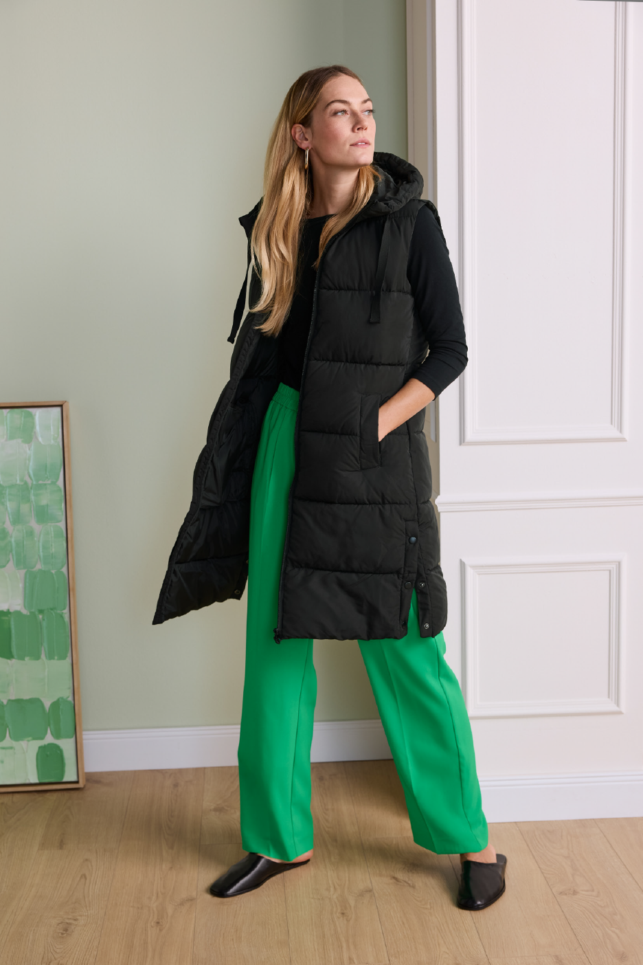 Γυναίκα με μακρύ μαύρο φουσκωτό γιλέκο, πράσινο παντελόνι και μαύρα παπούτσια.