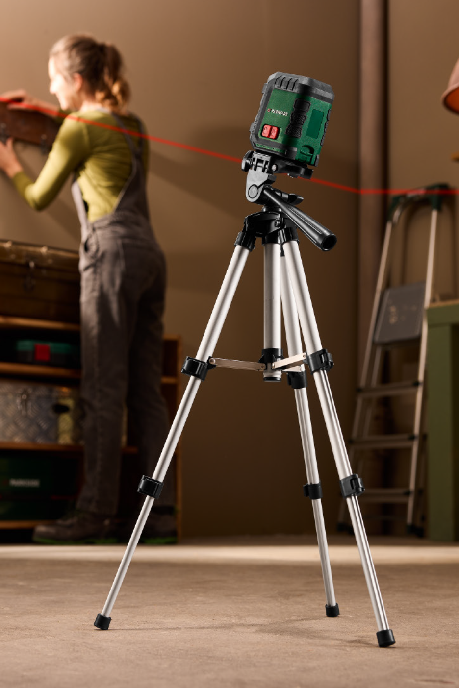 Γυναίκα χρησιμοποιεί λέιζερ αλφάδι σε τρίποδο για να κρεμάσει κάτι στον τοίχο.