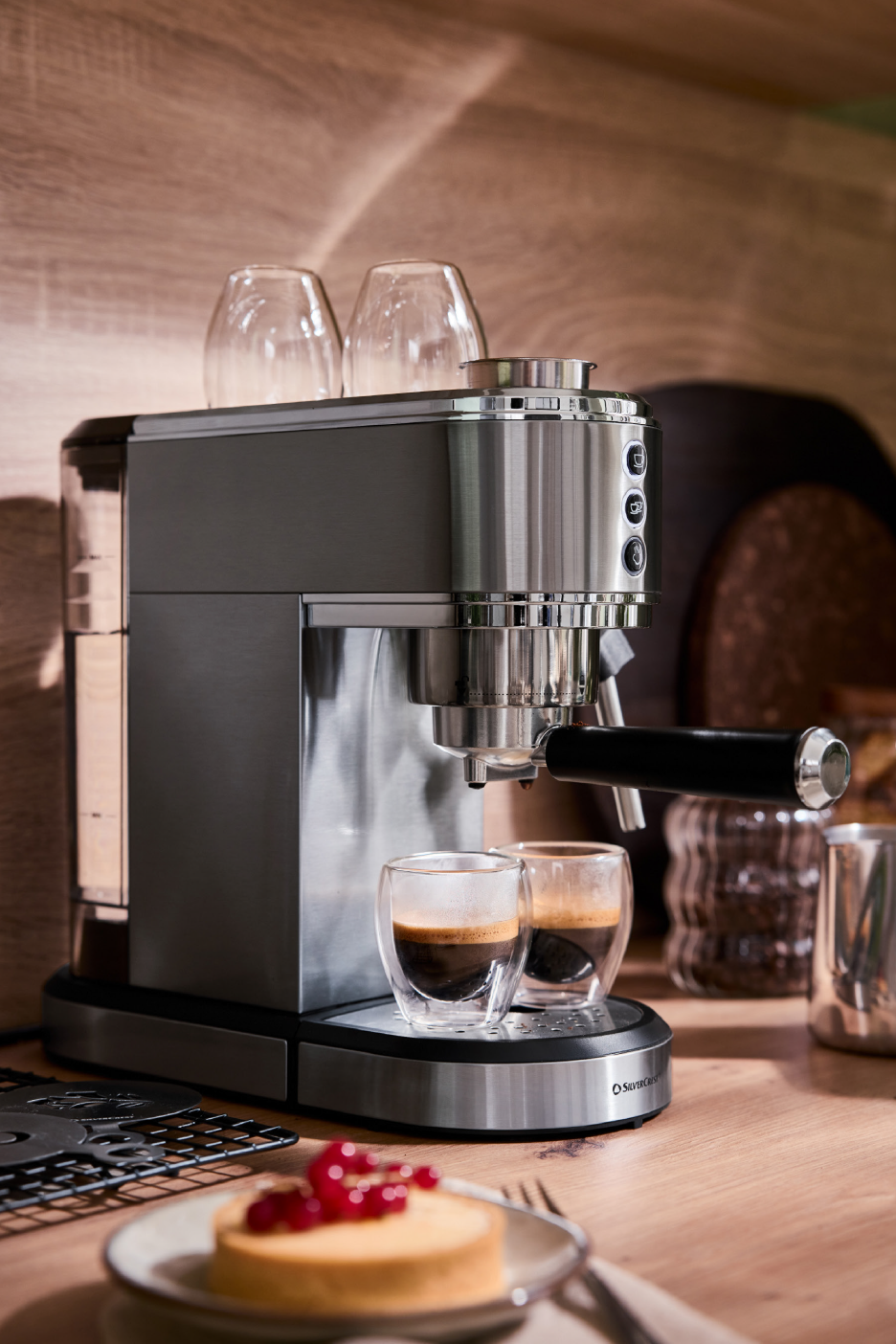 Μηχανή εσπρέσο με δύο φλιτζάνια καφέ και ένα γλυκό με κόκκινα φρούτα.