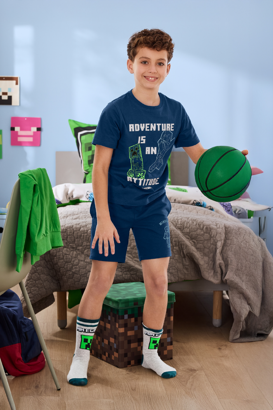 Αγόρι με μπλε μπλουζάκι και σορτς με θέμα παιχνιδιού, κρατώντας μια πράσινη μπάλα.