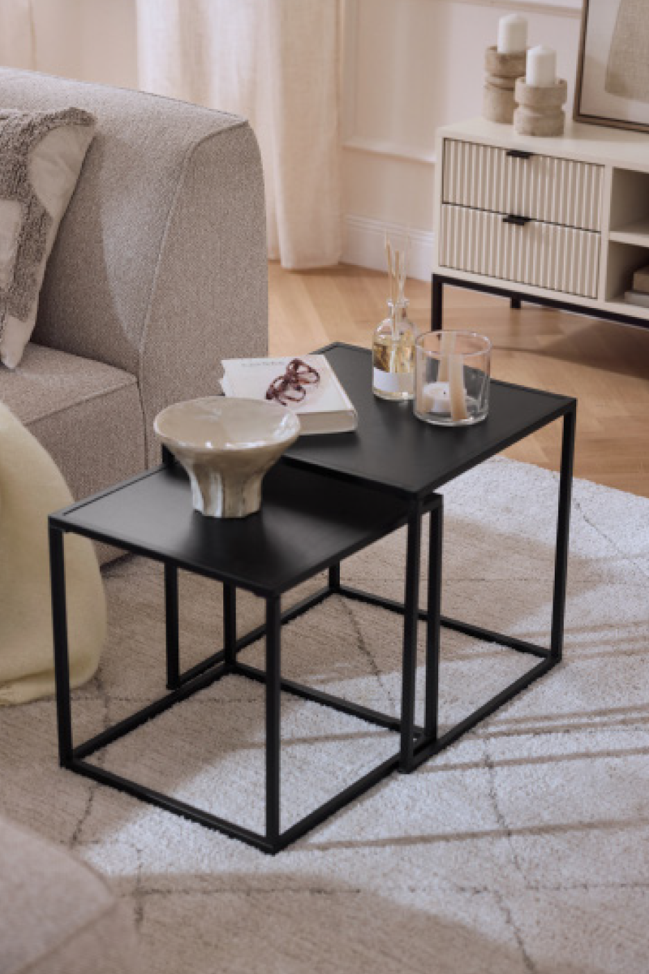 Μαύρα ένθετα τραπεζάκια σαλονιού με διακοσμητικά, δίπλα σε έναν καναπέ και ένα έπιπλο αποθήκευσης.