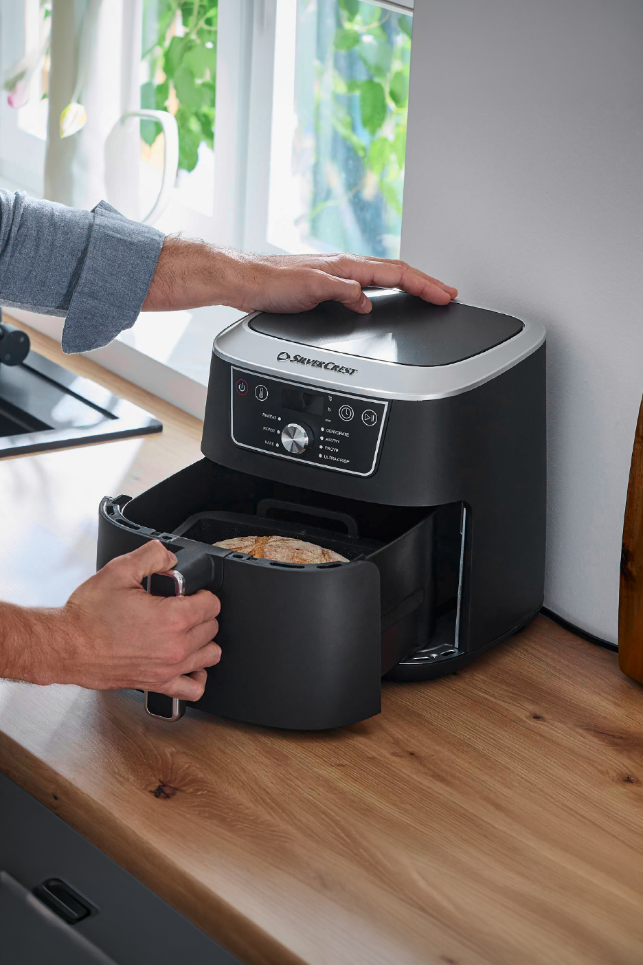 Άντρας βάζει ψωμί σε φριτέζα αέρος στην κουζίνα.