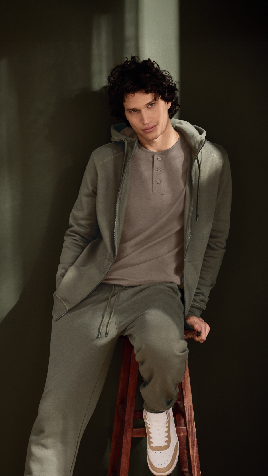 Άνδρας με χακί φούτερ με κουκούλα, μπλουζάκι Henley και ασορτί φόρμα.