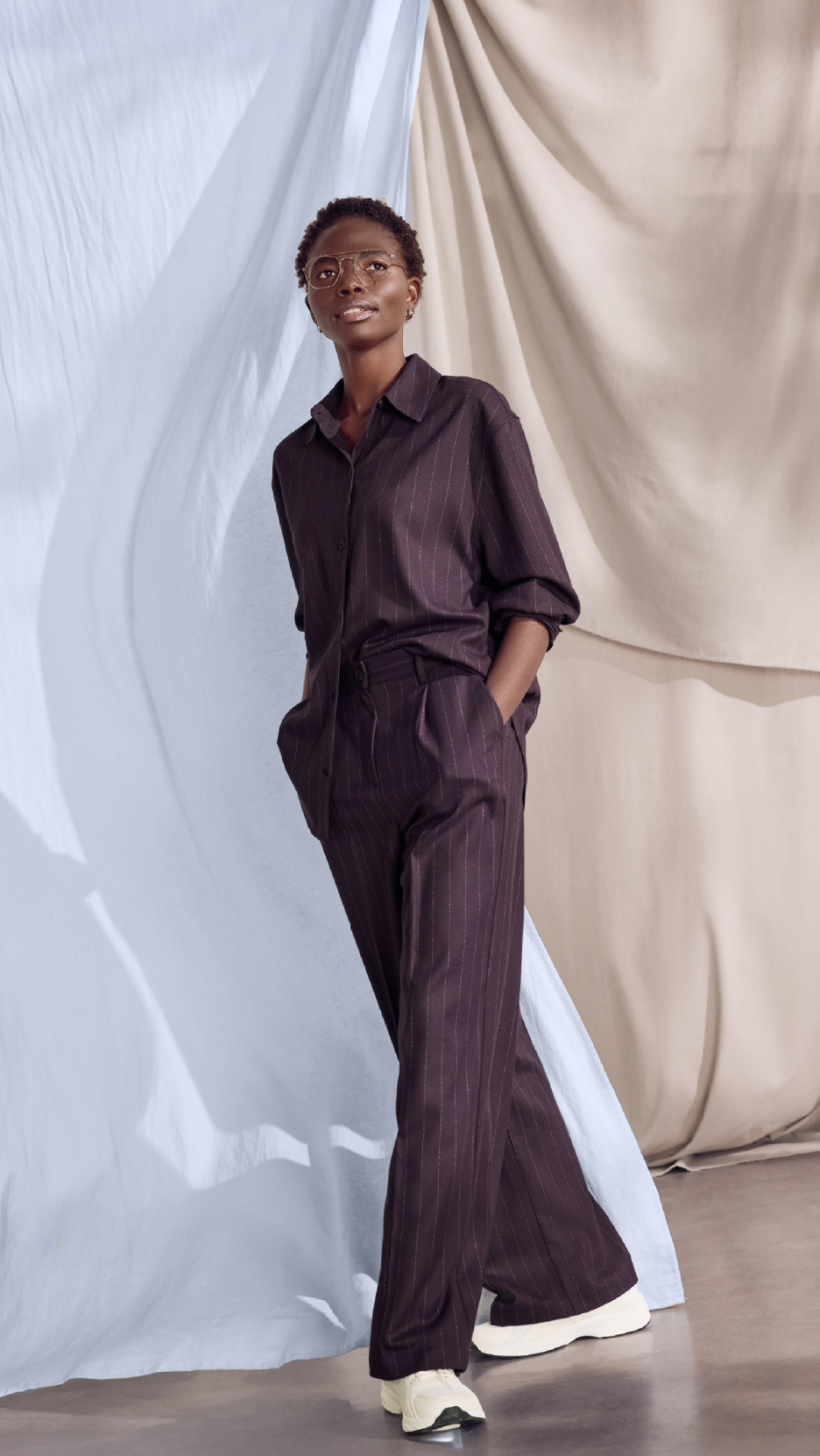 Γυναίκα με ριγέ σκούρο καφέ πουκάμισο και παντελόνι, με τα χέρια στις τσέπες.