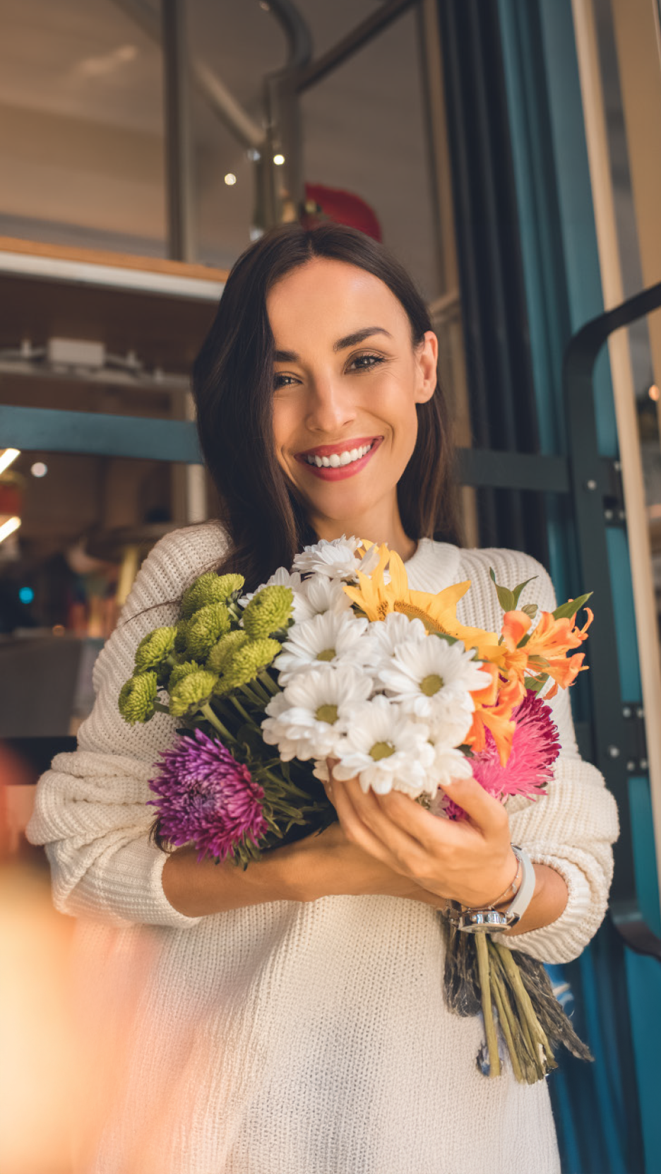 Μια χαμογελαστή γυναίκα κρατά μια πολύχρωμη ανθοδέσμη με φρέσκα λουλούδια.