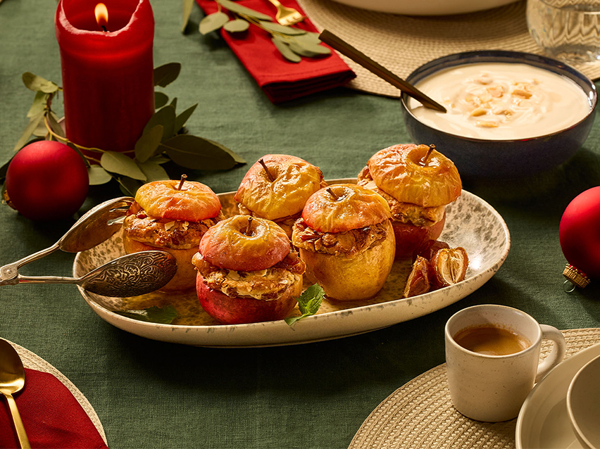 Ψητά μήλα γεμιστά με ξηρούς καρπούς, σε γιορτινό τραπέζι με κόκκινα στολίδια.