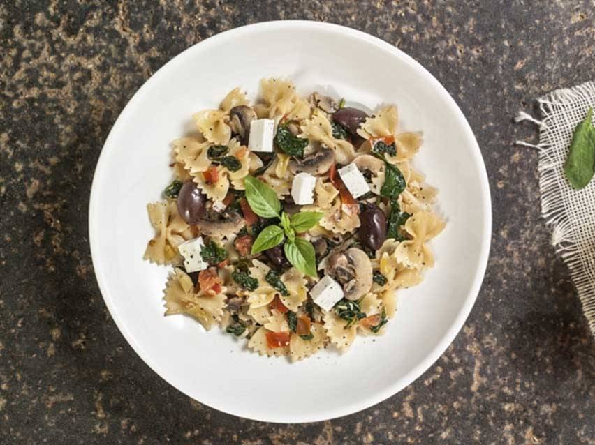 Πιάτο με ζυμαρικά farfalle, μανιτάρια, ελιές, σπανάκι και φέτα, γαρνιρισμένο με βασιλικό.