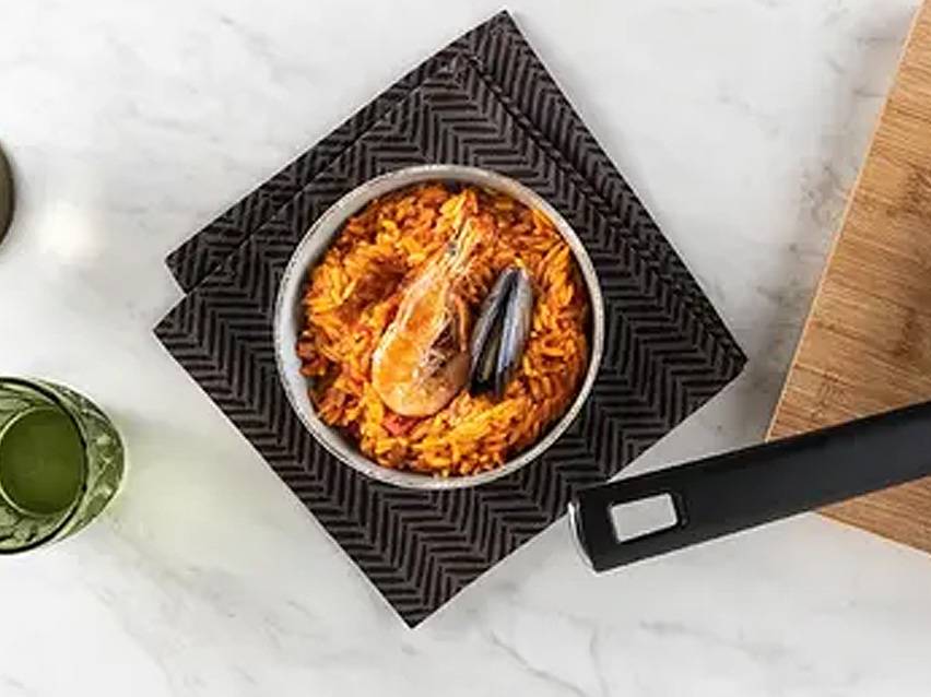 Παέγια με γαρίδες και μύδια σε μπολ, πάνω σε μαύρη πετσέτα κουζίνας.