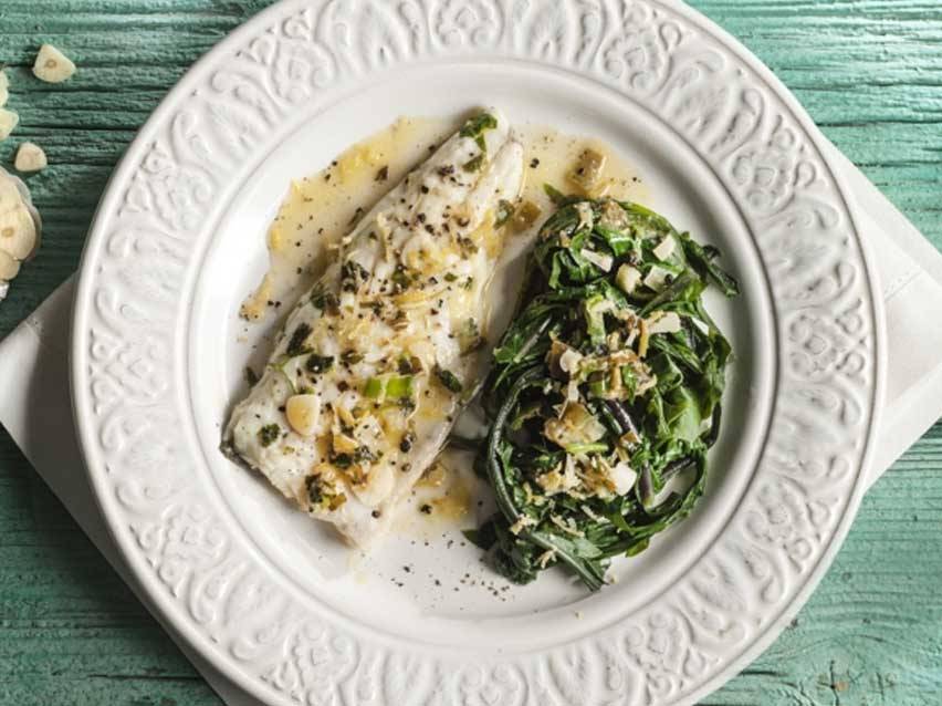 Φιλέτο ψαριού με σπανάκι και σάλτσα σκόρδου σε λευκό πιάτο.