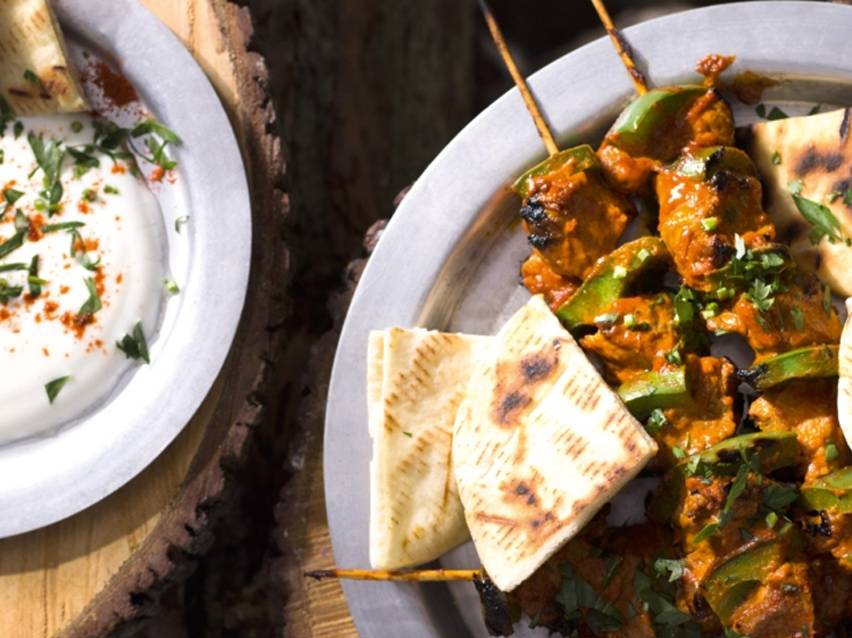 Σουβλάκια κοτόπουλου με πιπεριές, πίτες και σάλτσα γιαουρτιού σε ξύλινο φόντο.