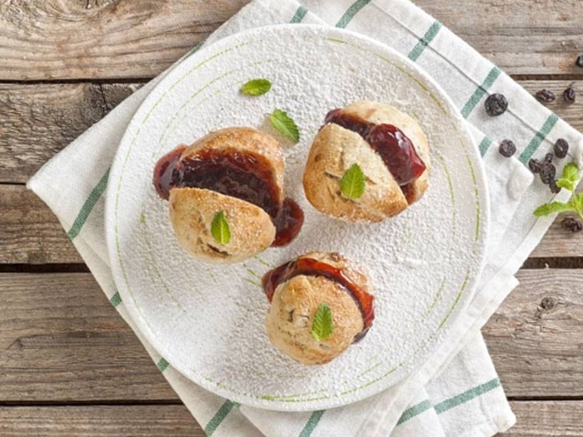 Σκονς με μαρμελάδα και φύλλα μέντας σε λευκό πιάτο, πασπαλισμένα με ζάχαρη άχνη.