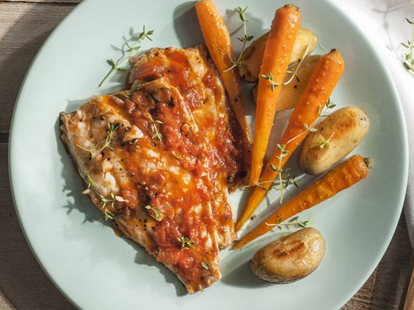 Ψητό ψάρι με σάλτσα ντομάτας, καρότα και πατάτες, γαρνιρισμένο με θυμάρι.